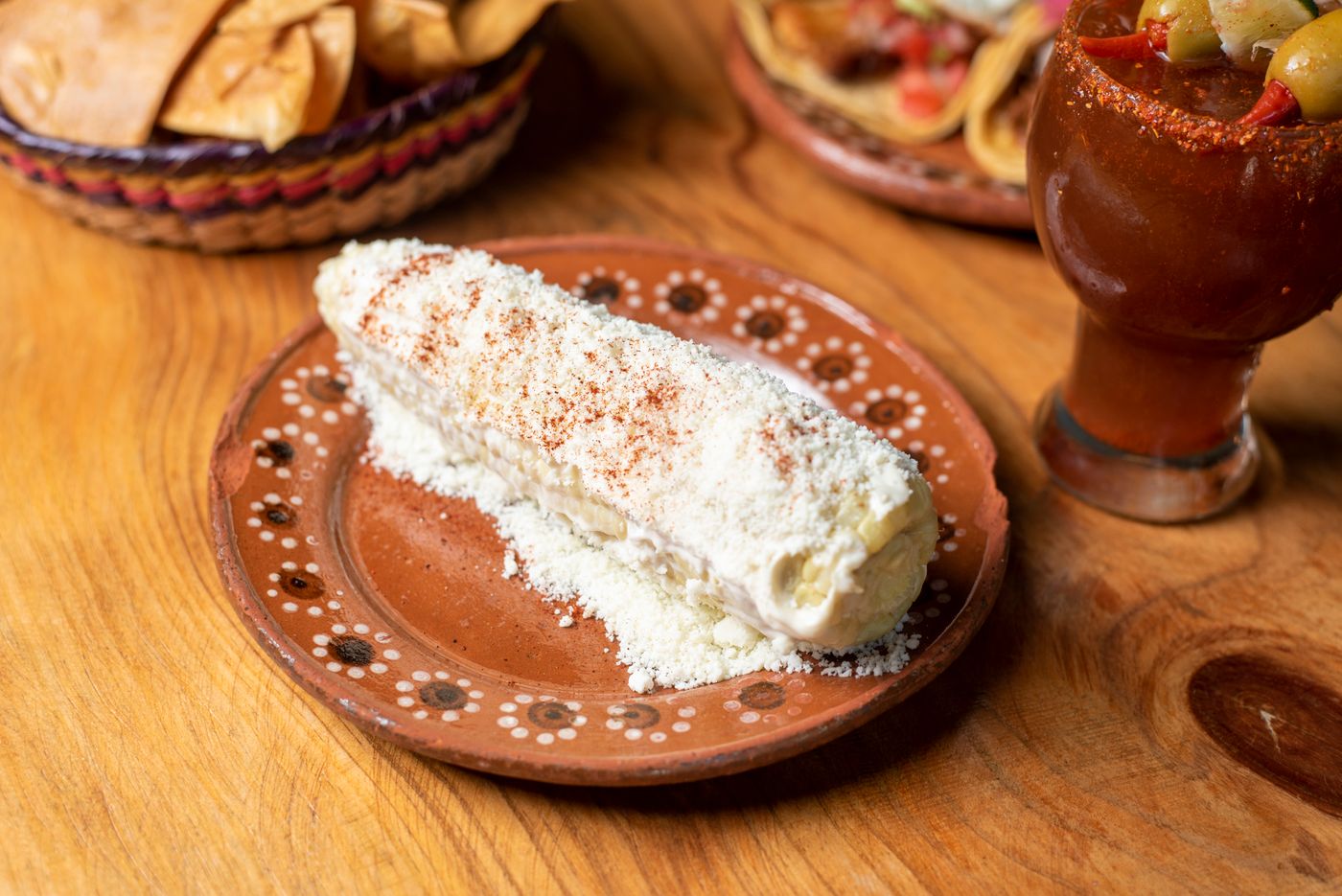 Elote dressed with crema and cheese on a terracotta plate