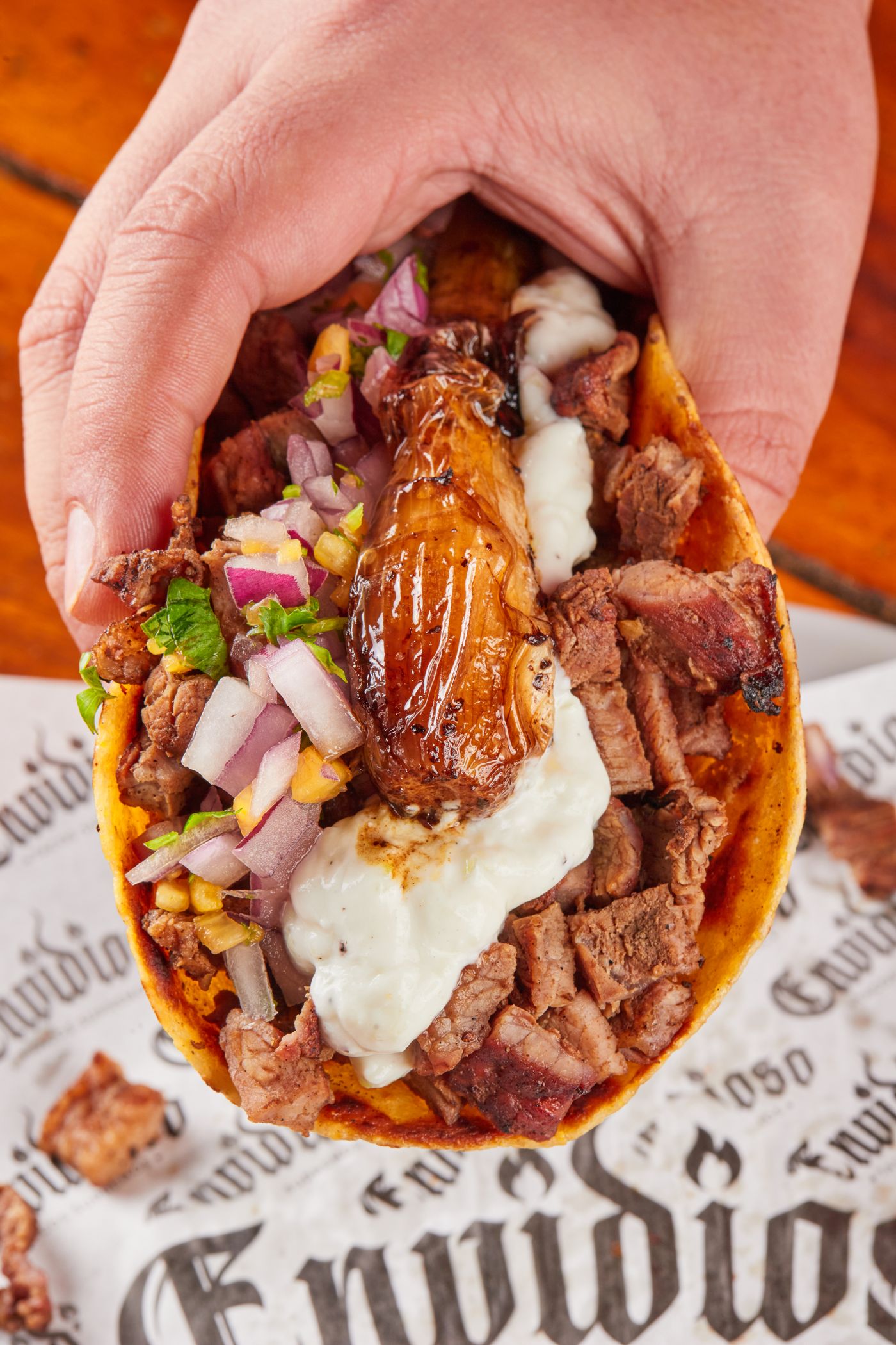 A hand lifting a stewed-beef taco loaded with onion and cilantro off butcher paper