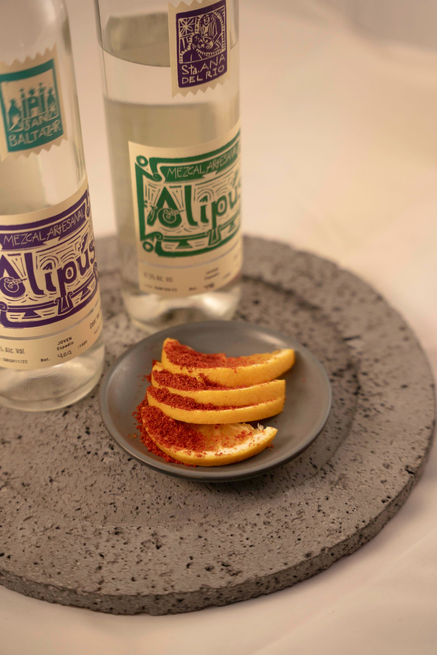 Mezcal bottles with seasoned orange slices on a stone plate