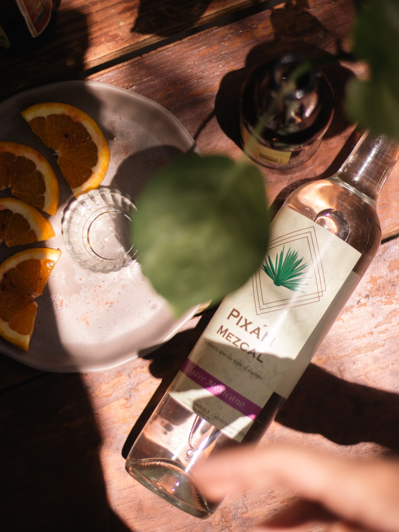 A pour of mezcal served with orange slices on a rustic table