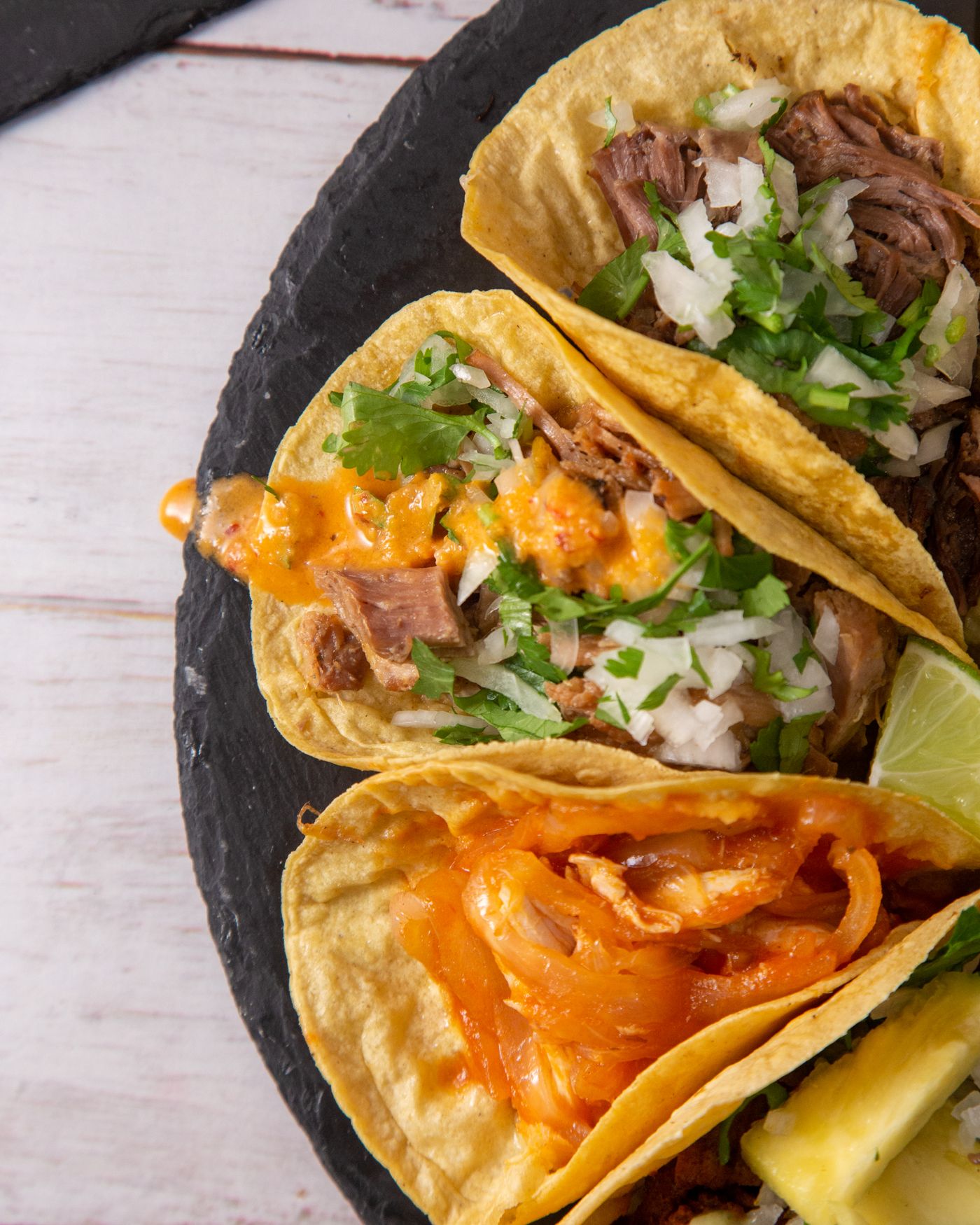 An assortment of tacos with bright toppings on dark slate