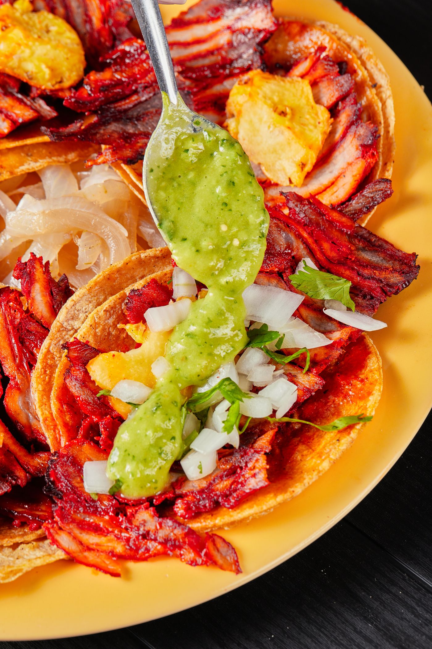 A loaded tostada topped with guacamole and stewed meat on a yellow plate