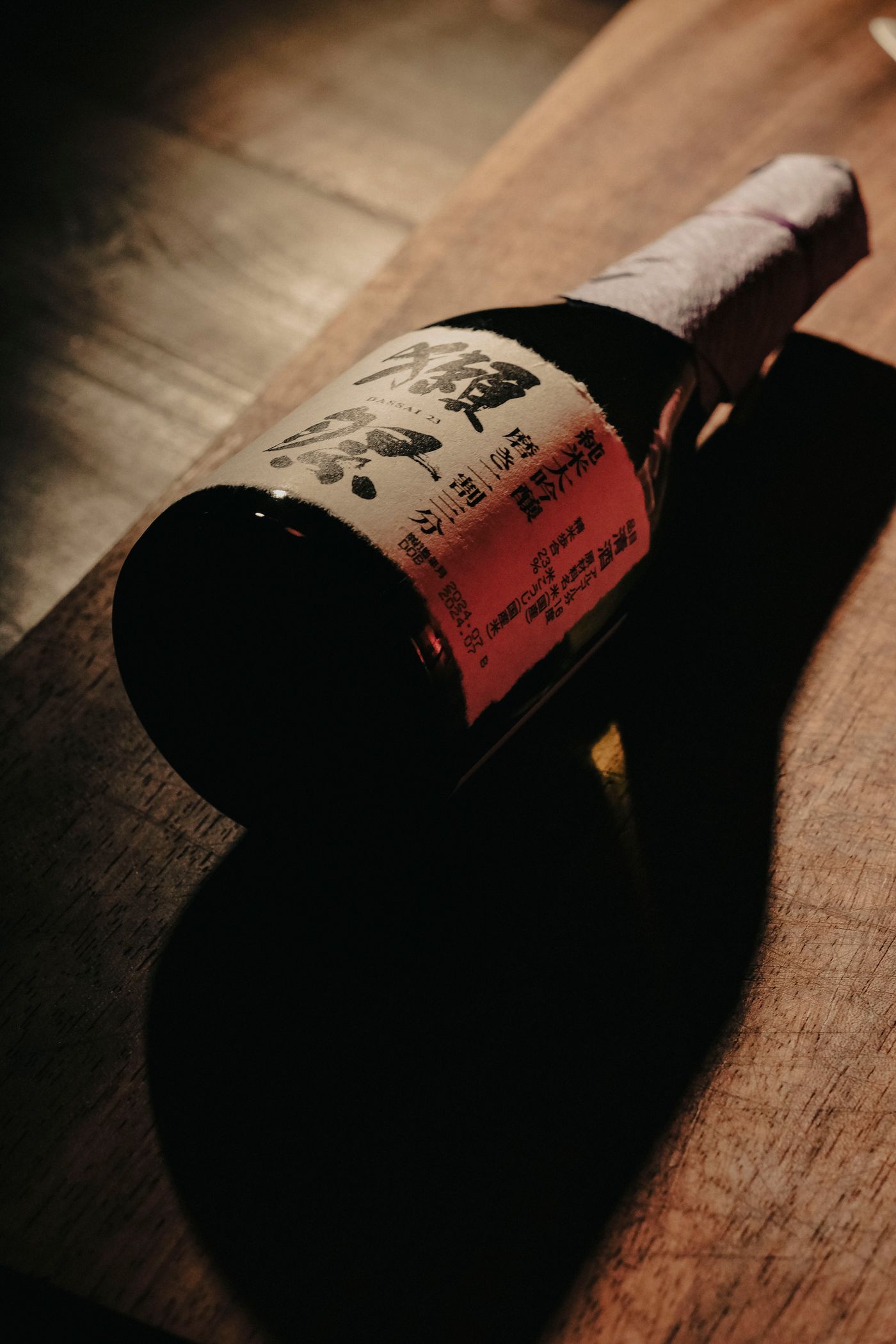 A dark bottle of premium sake lying on a wooden table in low, dramatic candlelight