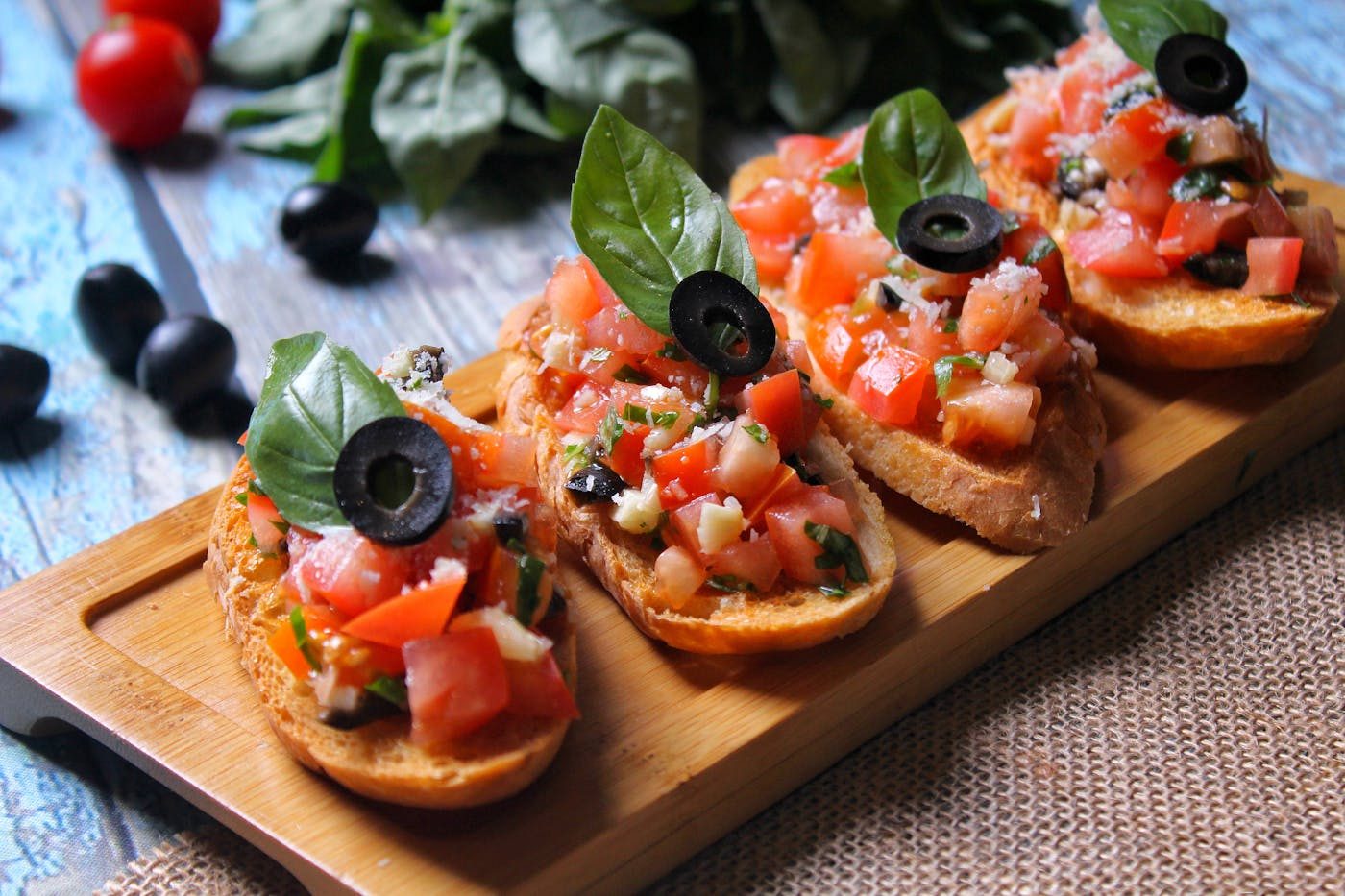 Bruschetta topped with diced tomato and olives on a wooden board