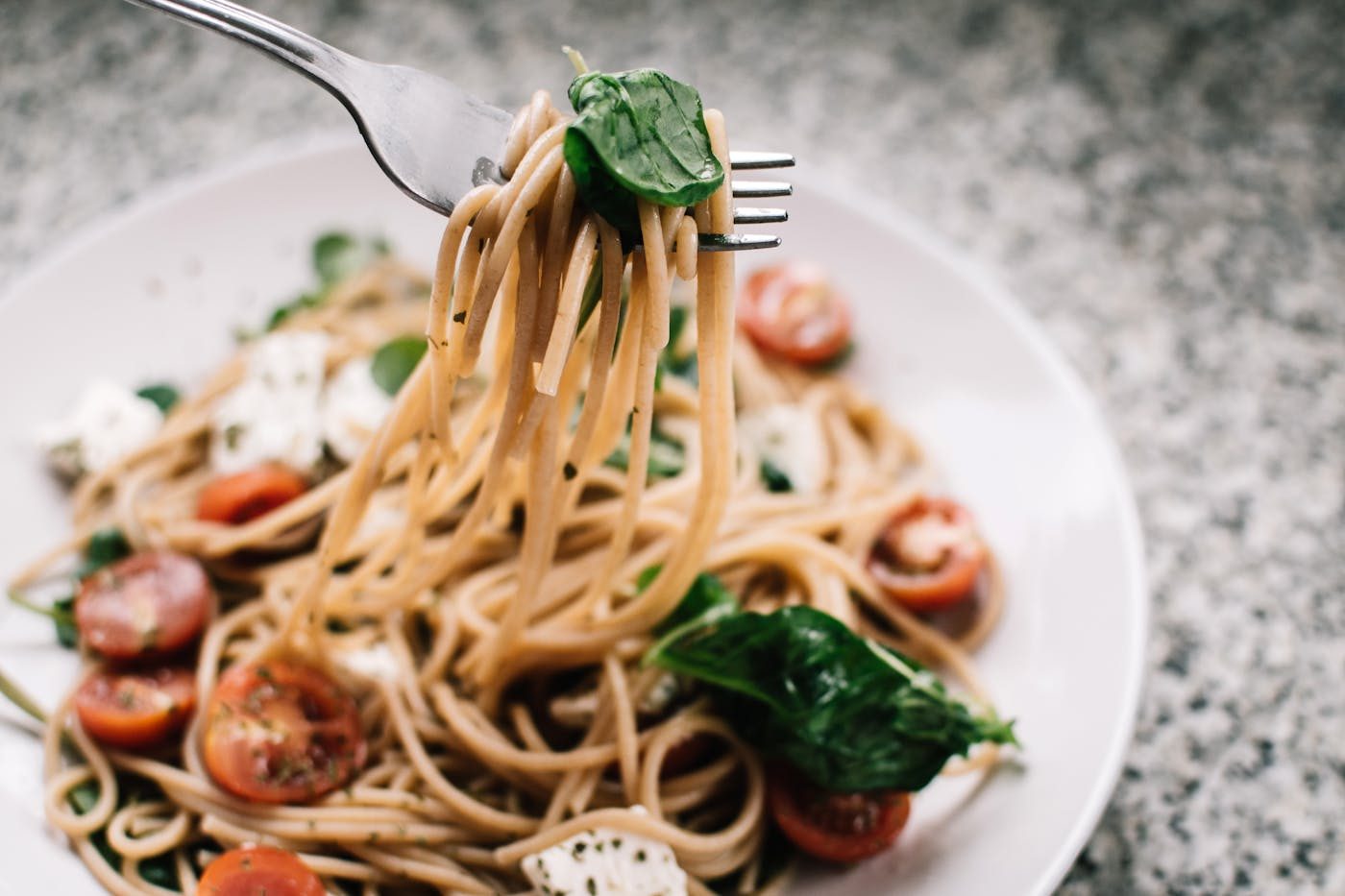 A fork lifting spaghetti tossed with cherry tomatoes and greens